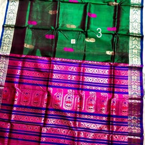 May include: A vibrant green and magenta silk saree featuring a wide, ornate border with intricate gold zari patterns, paisley motifs, and horizontal stripes. The main body displays scattered gold and magenta floral accents and the number 3.