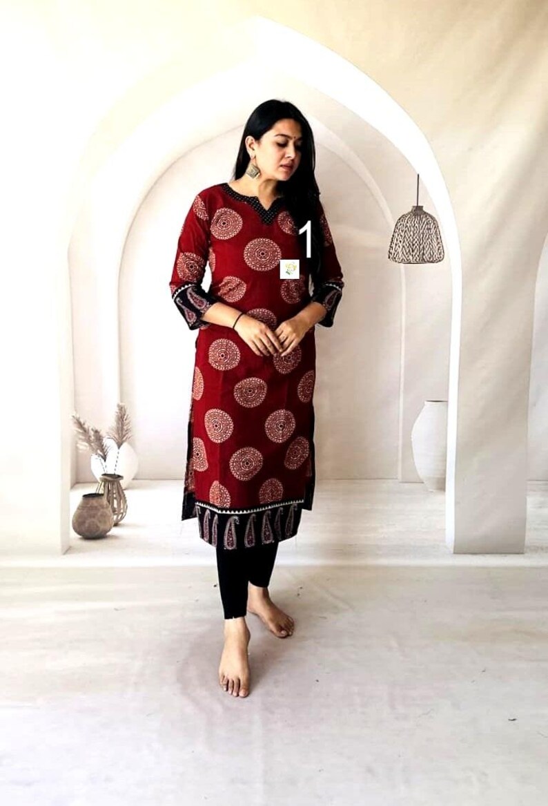Puede incluir: Un vestido t&uacute;nica burdeos con un estampado circular crema. El vestido tiene mangas tres cuartos con un estampado de cachemira negro y crema en los pu&ntilde;os. El escote y el dobladillo tambi&eacute;n presentan detalles en negro y crema. La modelo lleva leggings negros.