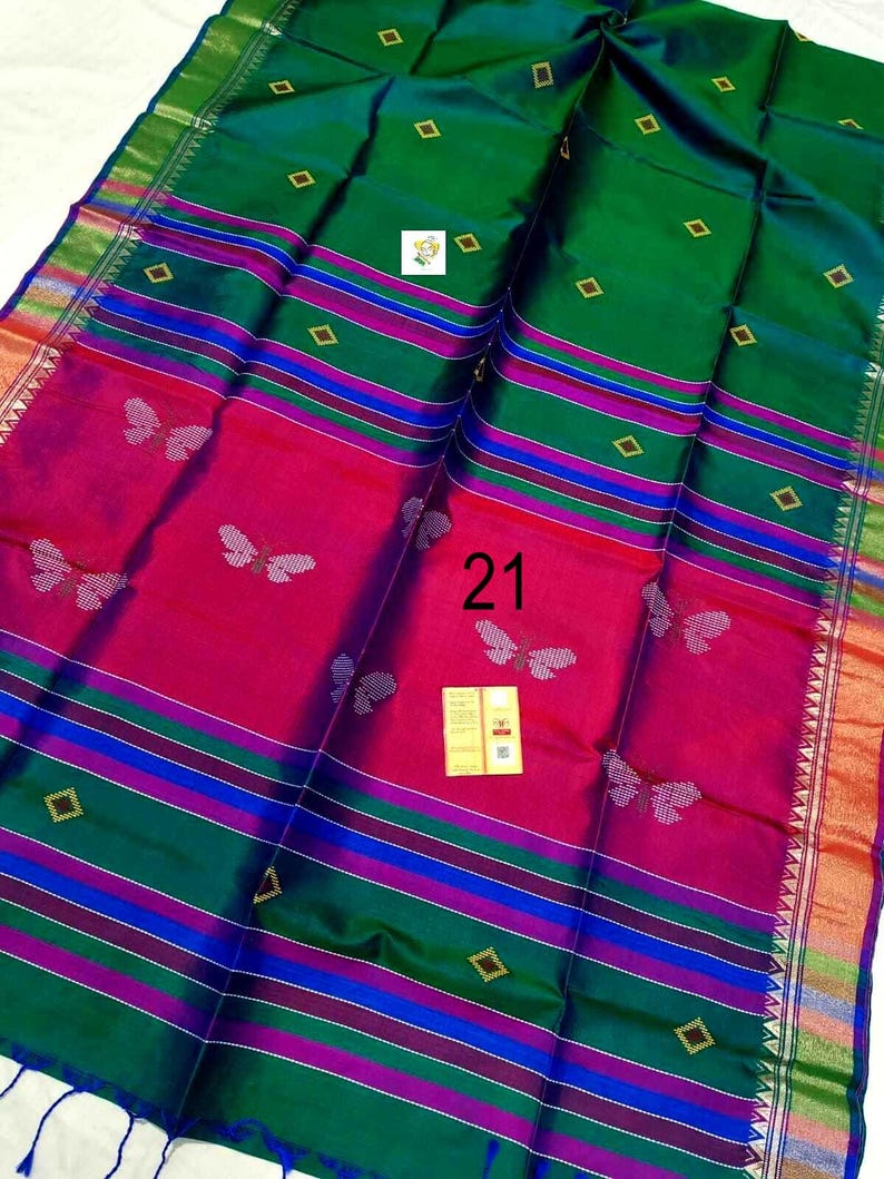 Puede incluir: Un sari verde y magenta con un patr&oacute;n repetido de mariposas, rayas horizontales en azul y morado, y peque&ntilde;os motivos de diamantes dorados. La tela muestra el n&uacute;mero 21 y una peque&ntilde;a etiqueta rectangular con texto en el centro de la pieza.