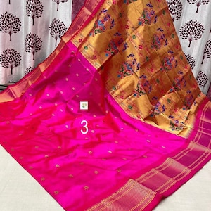 Op de afbeelding: Een levendige fuchsia roze sari met een grote gouden pallu met ingewikkelde veelkleurige pauw- en bloemmotieven. Het hoofdgedeelte van de stof is versierd met kleine gouden stervormige patronen en een brede rand met horizontale gouden strepen.
