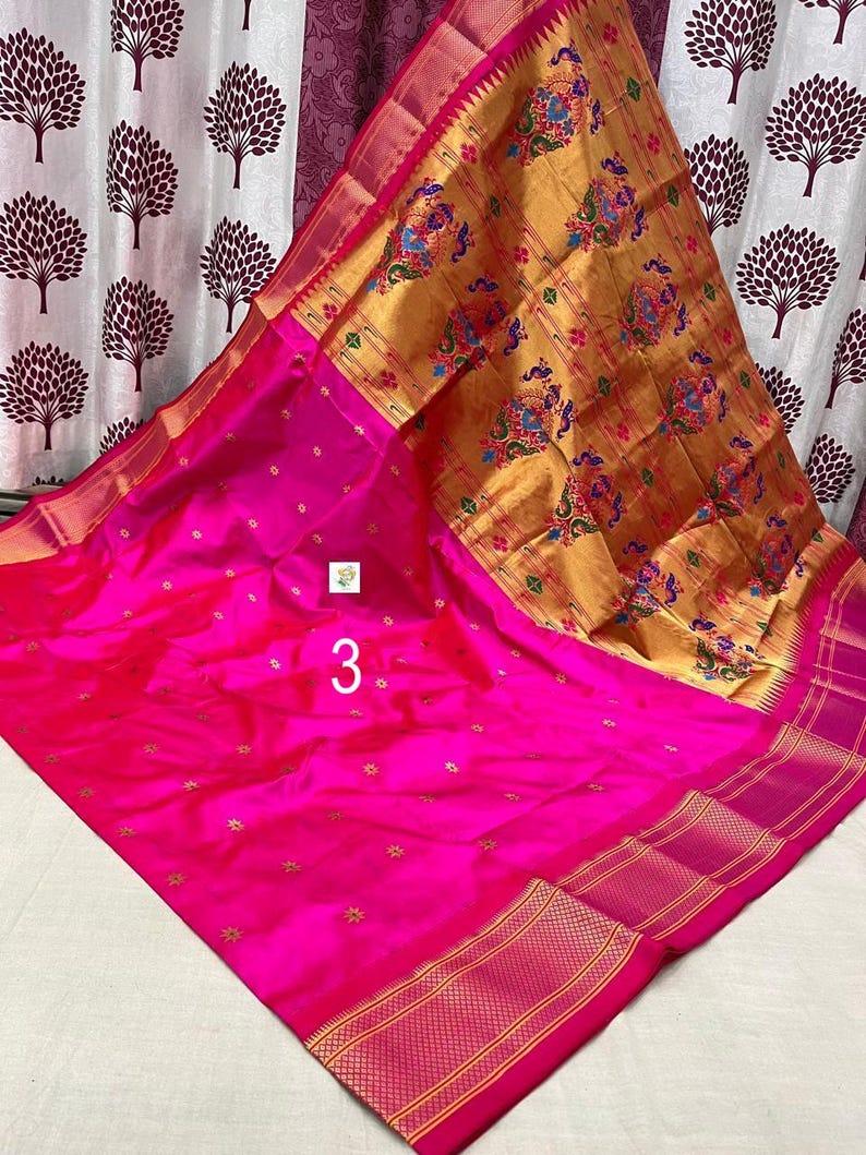 Op de afbeelding: Een levendige fuchsia roze sari met een grote gouden pallu met ingewikkelde veelkleurige pauw- en bloemmotieven. Het hoofdgedeelte van de stof is versierd met kleine gouden stervormige patronen en een brede rand met horizontale gouden strepen.