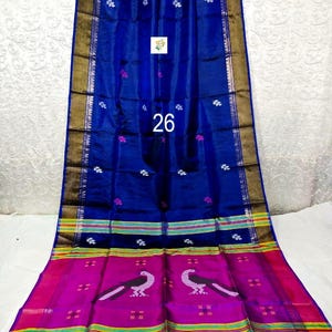 Puede incluir: Un sari azul real con un borde ancho magenta que presenta dos motivos de pavo real en blanco y negro. La tela muestra peque&ntilde;os patrones florales blancos en todo el cuerpo, rematado con ribetes met&aacute;licos dorados y rayas horizontales amarillas y verdes.