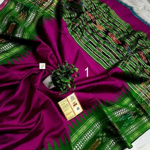May include: A vibrant magenta saree featuring a wide, deep green border with intricate ikat patterns and a metallic gold zari edge. The fabric displays a smooth texture, accented by a small green plant and a rectangular product tag labeled with the number 1.