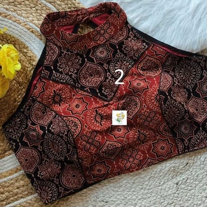 Puede incluir: Un top halter de patr&oacute;n rojo y negro con una abertura de ojo de cerradura en la espalda. El top tiene un dise&ntilde;o geom&eacute;trico con el n&uacute;mero "2" impreso en la parte delantera.