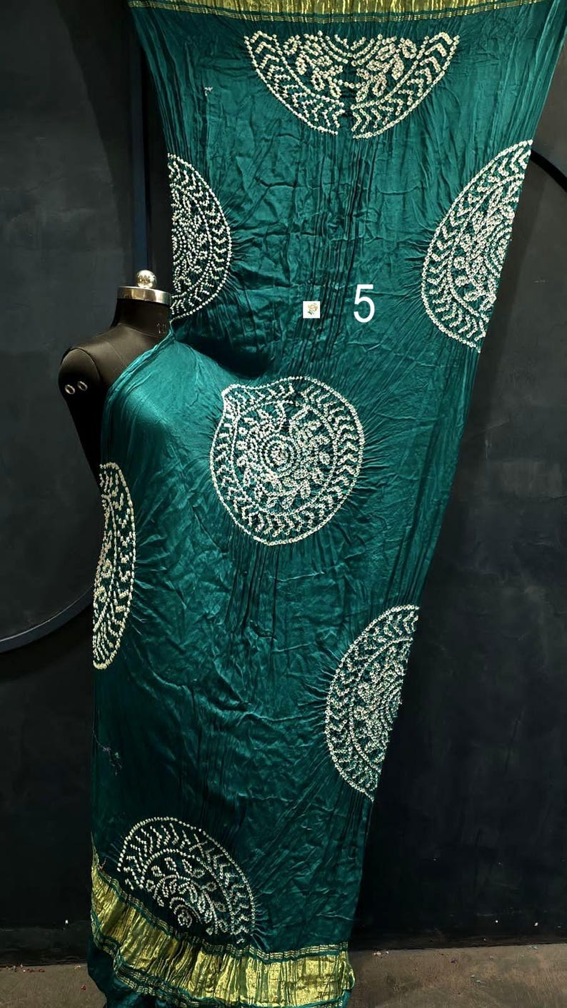 May include: A dark teal fabric drape featuring white circular patterns with intricate detailing and a crinkled texture. The fabric has a metallic gold border at the bottom and includes the number 5 printed in white near the centre of the material.