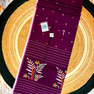 May include: A deep purple fabric textile featuring a light pink border, small scattered diamond-shaped motifs in green, orange, and pink, horizontal white stripes, and a large floral pattern with green and orange leaves and pink flowers, labeled 7.