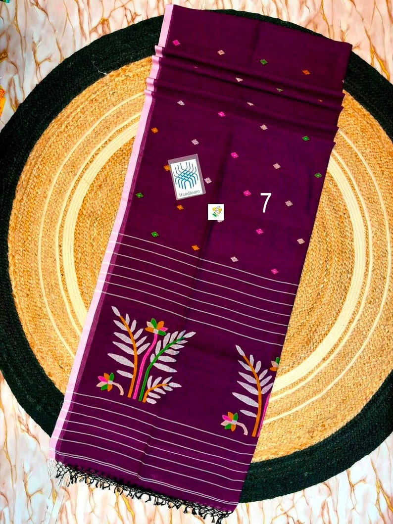 May include: A deep purple fabric textile featuring a light pink border, small scattered diamond-shaped motifs in green, orange, and pink, horizontal white stripes, and a large floral pattern with green and orange leaves and pink flowers, labeled 7.