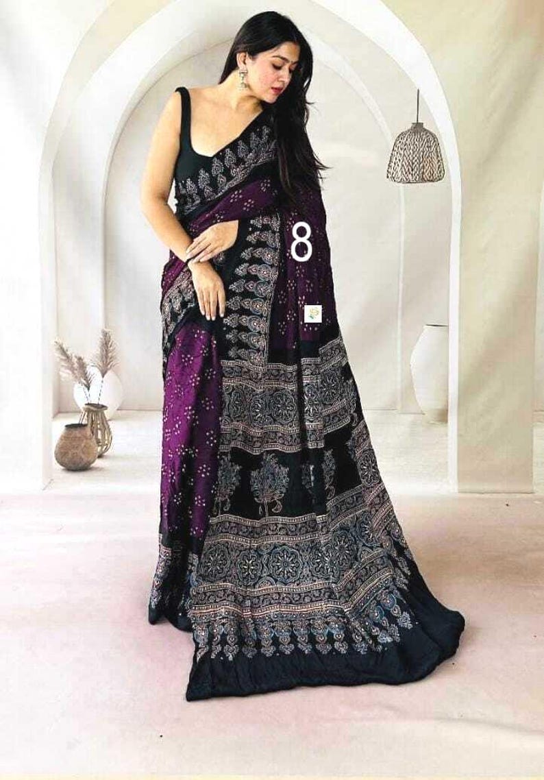May include: A black and deep purple saree featuring a sleeveless blouse and a long, flowing drape. The fabric is adorned with intricate, repeating white and light-colored floral and geometric patterns throughout the body and the wide border.