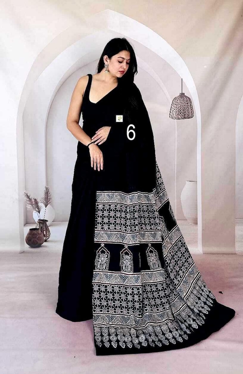 Puede incluir: Un sari negro que presenta una blusa sin mangas y un largo drapeado adornado con un patr&oacute;n estampado en blanco. El dise&ntilde;o intrincado incluye formas geom&eacute;tricas y motivos arquitect&oacute;nicos en el borde, con el n&uacute;mero 6 impreso en la tela.