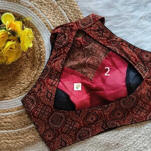 Puede incluir: Una blusa de estampado rojo y negro con un escote de ojo de cerradura en la espalda. La blusa tiene un ribete negro y un forro rojo. El n&uacute;mero "2" est&aacute; escrito en el forro.