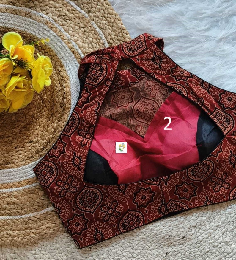 Puede incluir: Una blusa de estampado rojo y negro con un escote de ojo de cerradura en la espalda. La blusa tiene un ribete negro y un forro rojo. El n&uacute;mero "2" est&aacute; escrito en el forro.