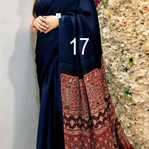 Puede incluir: Un sari azul marino oscuro con un cuerpo liso y de color s&oacute;lido, y un pallu ancho y contrastante con intrincados patrones geom&eacute;tricos y florales en rojo, negro y blanco. El n&uacute;mero 17 est&aacute; impreso en blanco en el centro de la tela.