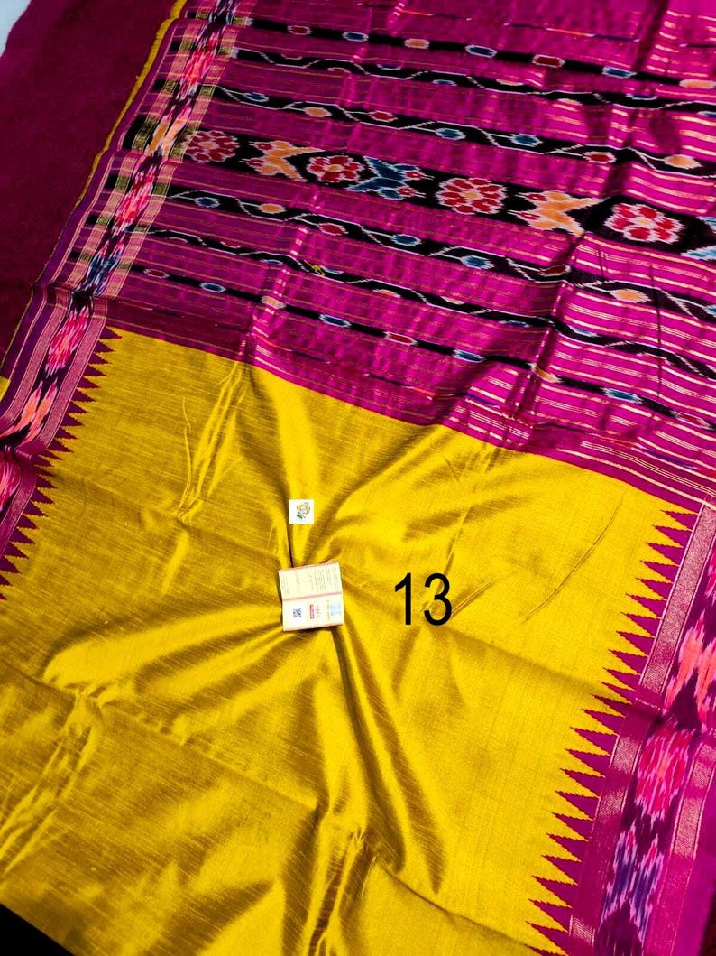 May include: A vibrant textile with a yellow and fuchsia color scheme. The fabric features intricate patterns in shades of pink, black, and orange. The number "13" is visible on the yellow portion of the textile. The edges are adorned with a decorative border.