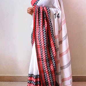 K&ouml;nnte beinhalten: Wei&szlig;er Sari mit rotem und schwarzem Zickzackmuster-Rand und Akzenten. Der Sari hat einen roten Rand und ein Streifendesign auf dem Pallu. Die Nummer "14" ist auf dem Sari sichtbar.