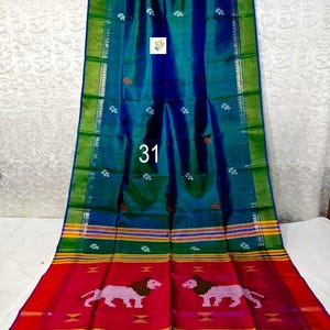 Puede incluir: Un tejido largo y rectangular con un centro iridiscente azul y verde intenso con peque&ntilde;os motivos florales blancos. El borde muestra rayas horizontales en amarillo, verde y rojo, con un patr&oacute;n repetitivo de dos figuras de leones rosas.