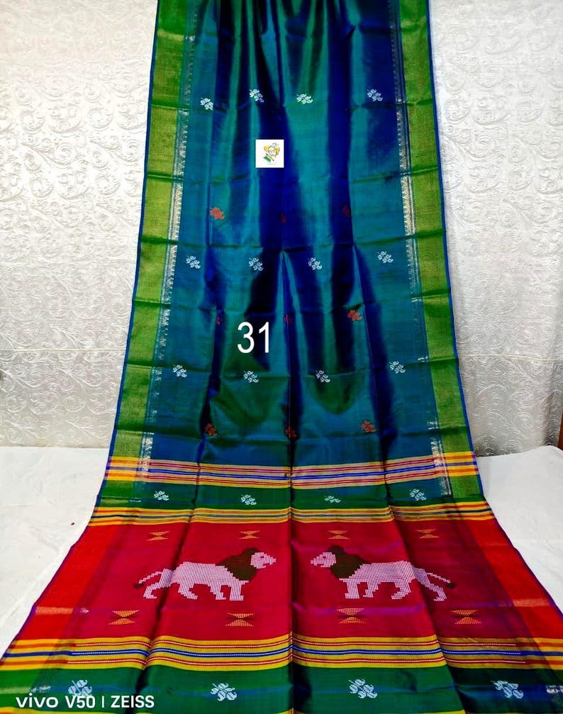 Puede incluir: Un tejido largo y rectangular con un centro iridiscente azul y verde intenso con peque&ntilde;os motivos florales blancos. El borde muestra rayas horizontales en amarillo, verde y rojo, con un patr&oacute;n repetitivo de dos figuras de leones rosas.