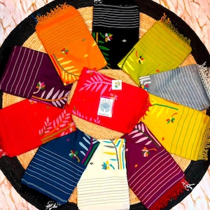 May include: A collection of ten rectangular fabric scarves arranged in a circular pattern. Each scarf features horizontal stripes, a floral motif, and fringed edges. The colors include orange, black, lime green, gray, red, yellow, dark blue, white, and purple.