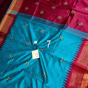 May include: A colourful textile in teal and maroon. It features small, embroidered square patterns in yellow, blue, and green. The design includes a border with a zigzag pattern and striped accents. The number "7" is visible.