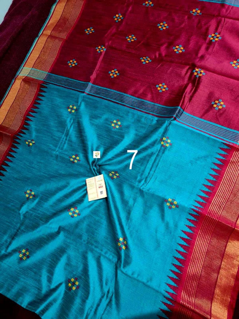 May include: A colourful textile in teal and maroon. It features small, embroidered square patterns in yellow, blue, and green. The design includes a border with a zigzag pattern and striped accents. The number "7" is visible.