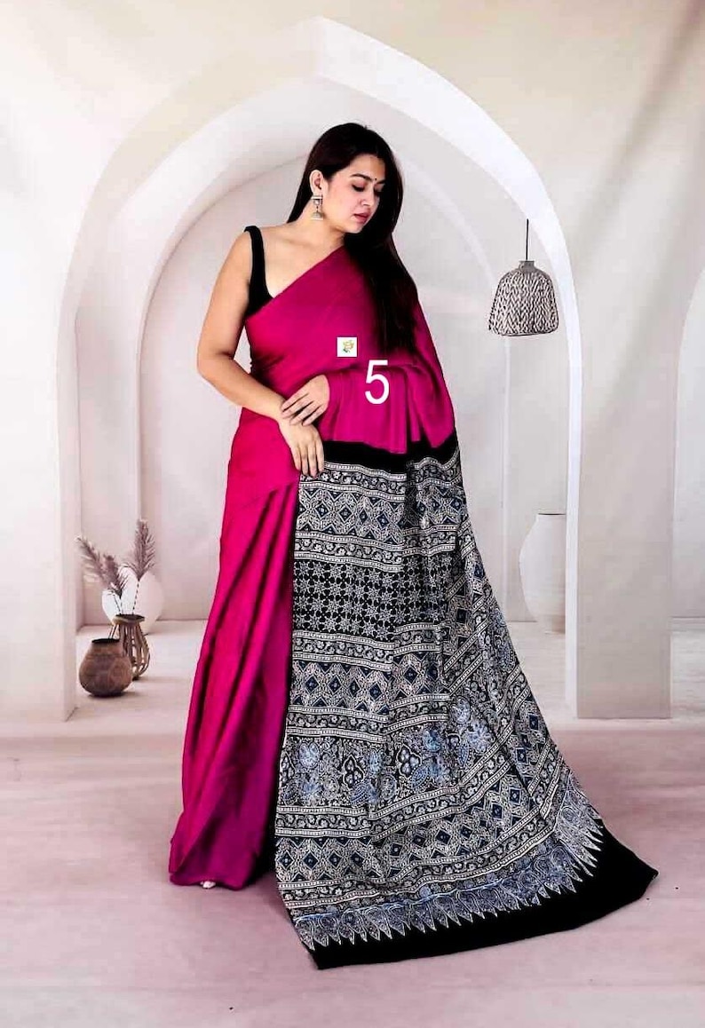 Puede incluir: Un sari magenta que presenta un drapeado de color s&oacute;lido y un pallu negro en contraste adornado con intrincados patrones geom&eacute;tricos blancos y azules. La prenda incluye una blusa negra sin mangas y muestra el n&uacute;mero 5 en la tela.