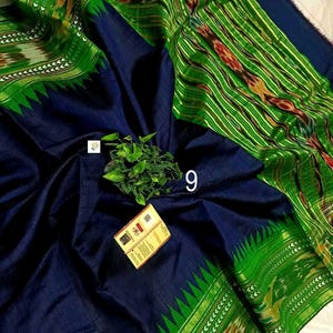 May include: A dark navy blue fabric with a vibrant green border featuring intricate ikat patterns and a serrated edge. The textile displays a woven texture, a small green plant sprig, the number 9, and a rectangular product tag with text.