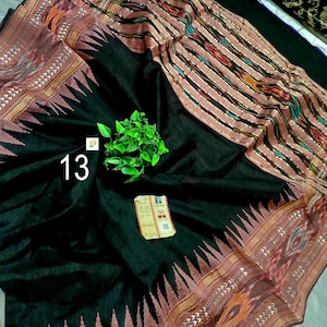 May include: A black textile fabric featuring a wide border with a repeating triangular pattern in muted red and gold. The fabric includes a section with vertical stripes in red, black, and gold, and displays the number 13 and a small tag.