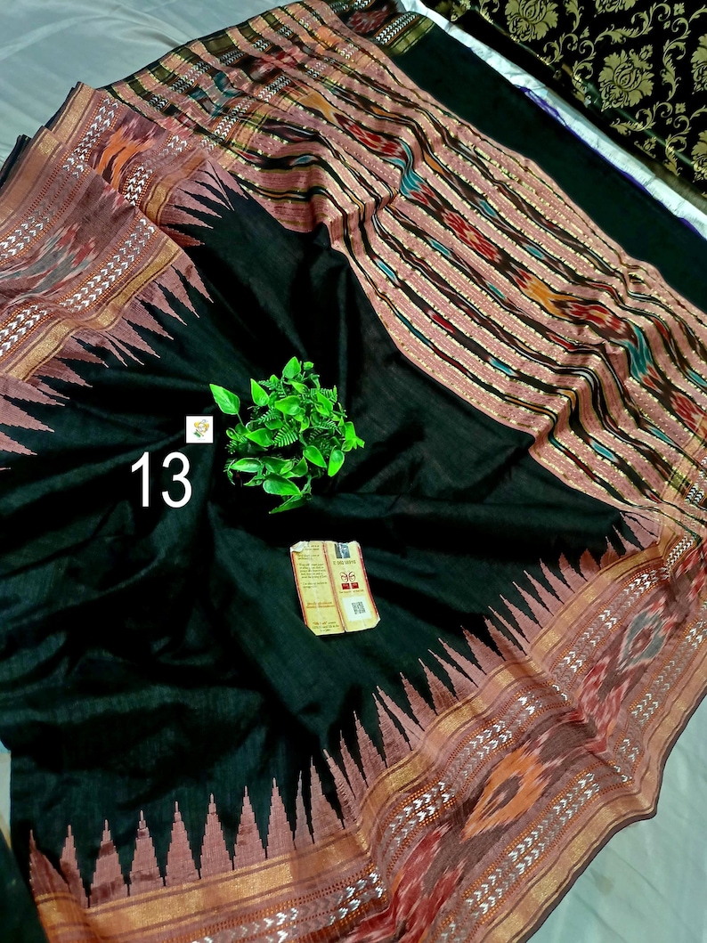 May include: A black textile fabric featuring a wide border with a repeating triangular pattern in muted red and gold. The fabric includes a section with vertical stripes in red, black, and gold, and displays the number 13 and a small tag.