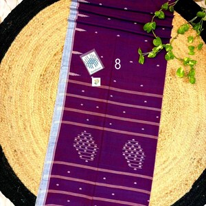 May include: A deep purple rectangular textile featuring horizontal white stripes, small white dot patterns, and two larger oval-shaped motifs. The fabric has a light blue border on one side, a red fringed edge at the bottom, and a small tag labeled 8.