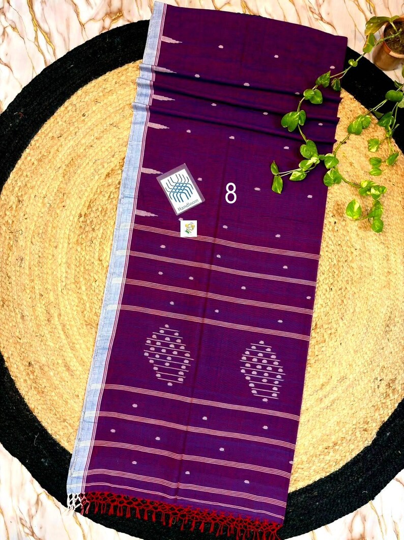 May include: A deep purple rectangular textile featuring horizontal white stripes, small white dot patterns, and two larger oval-shaped motifs. The fabric has a light blue border on one side, a red fringed edge at the bottom, and a small tag labeled 8.