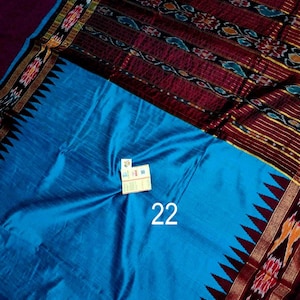 May include: A vibrant blue textile with a patterned border in shades of red, gold, and black. The textile features a repeating geometric design and the number "22" in white. The fabric has a silky sheen.
