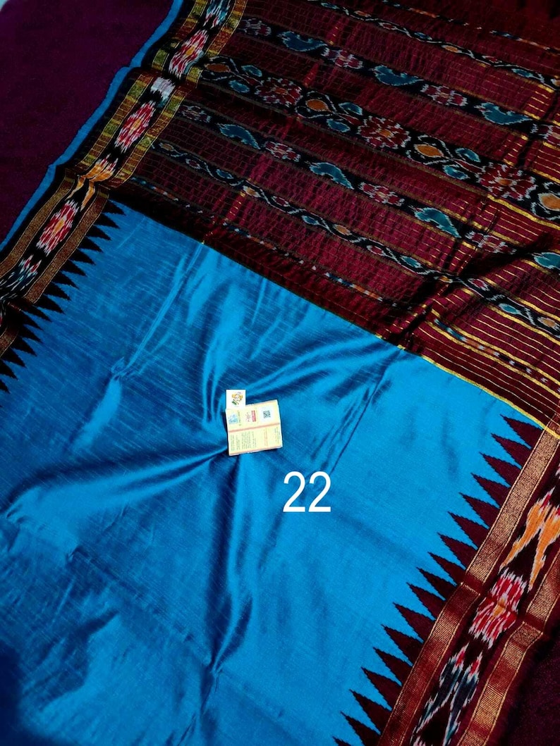 May include: A vibrant blue textile with a patterned border in shades of red, gold, and black. The textile features a repeating geometric design and the number "22" in white. The fabric has a silky sheen.