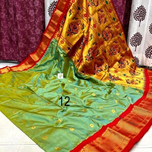 Op de afbeelding: Een lichtgroene sari met kleine gele bloemenborduursels en een brede, felgele pallu met ingewikkelde veelkleurige pauwen- en bloemmotieven. Het kledingstuk is afgewerkt met een opvallende rode rand en het cijfer 12 in het zwart gedrukt.