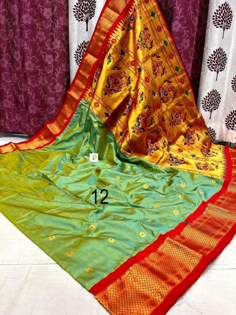 Op de afbeelding: Een lichtgroene sari met kleine gele bloemenborduursels en een brede, felgele pallu met ingewikkelde veelkleurige pauwen- en bloemmotieven. Het kledingstuk is afgewerkt met een opvallende rode rand en het cijfer 12 in het zwart gedrukt.
