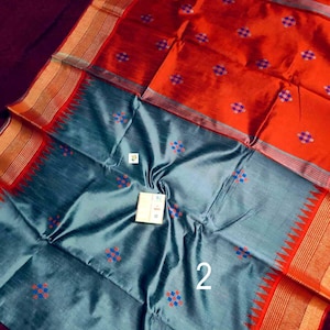 May include: A striking orange and grey saree with a detailed design. The saree features a pattern of small, colourful squares and intricate borders. The number "2" is visible on the fabric.