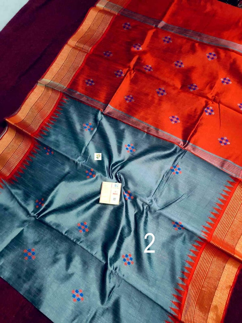 May include: A striking orange and grey saree with a detailed design. The saree features a pattern of small, colourful squares and intricate borders. The number "2" is visible on the fabric.