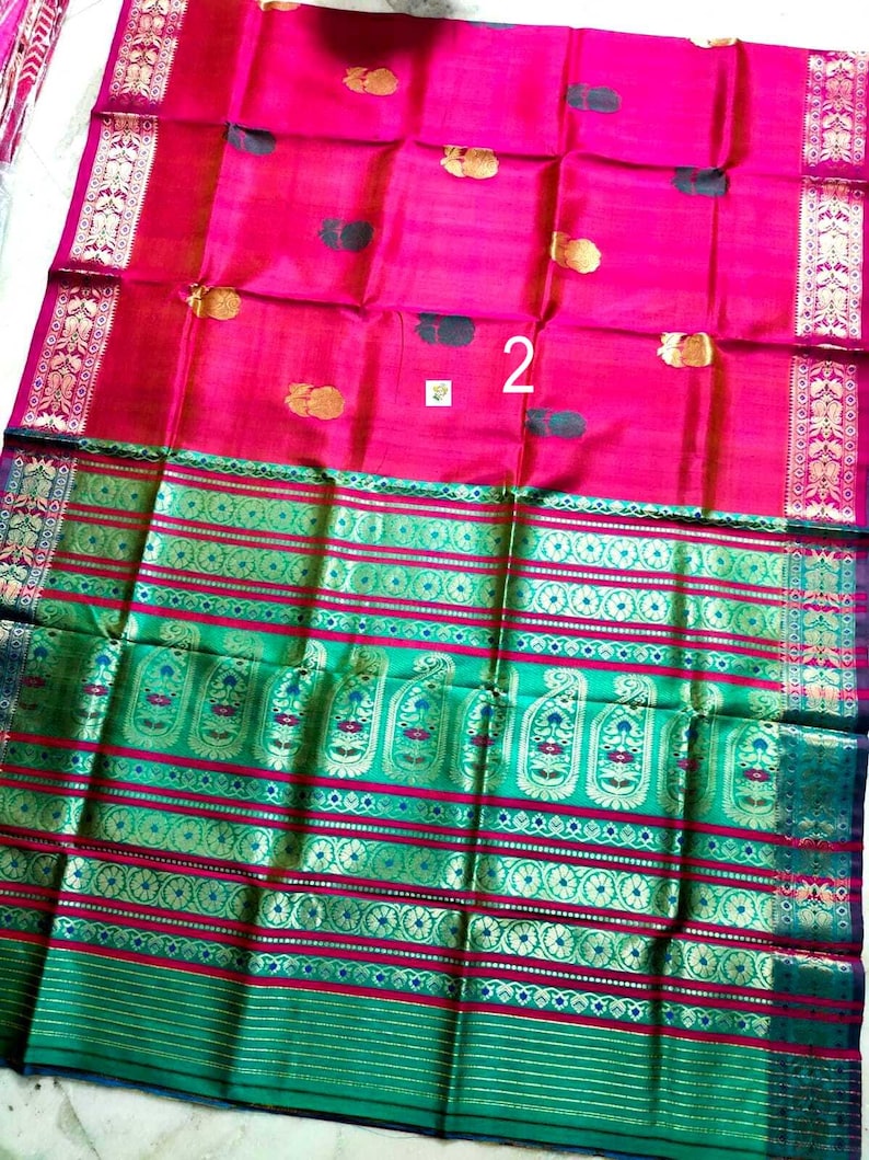 May include: A vibrant fuchsia pink saree featuring scattered gold and dark green floral motifs. The fabric includes a wide, ornate border in emerald green and gold with intricate paisley patterns and horizontal stripes. The number 2 is visible.
