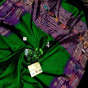 May include: A vibrant emerald green saree featuring a wide purple border with intricate ikat patterns in white, red, and yellow. The fabric displays a smooth texture with a prominent number 4 printed on the surface and a small attached product tag.