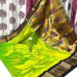 Op de afbeelding: Een fel limoengroene sari met een brede gouden rand met ingewikkelde bloemmotieven in roze, oranje en groen. De stof heeft een gladde afwerking met kleine verspreide gouden motieven en een opvallende zwarte rand langs de zijkanten. Het cijfer 6 is zichtbaar.