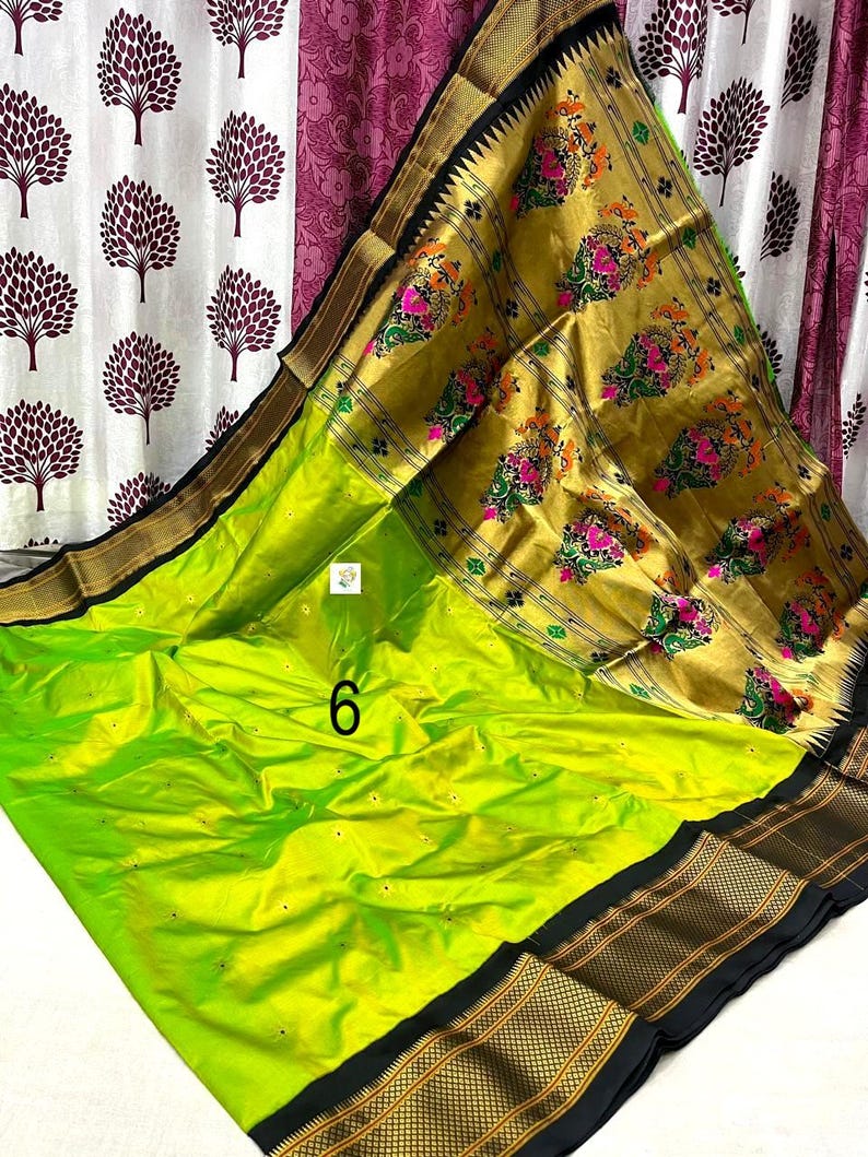 Op de afbeelding: Een fel limoengroene sari met een brede gouden rand met ingewikkelde bloemmotieven in roze, oranje en groen. De stof heeft een gladde afwerking met kleine verspreide gouden motieven en een opvallende zwarte rand langs de zijkanten. Het cijfer 6 is zichtbaar.