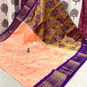 Op de afbeelding: Een perzikkleurige sari met een brede paarse rand met gouden geometrische patronen. De pallu is goudkleurig met kleurrijke pauwenmotieven. Het hoofdgedeelte heeft kleine verspreide bloemenborduursels en het cijfer 4 is op de stof gedrukt.