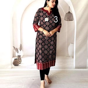 Puede incluir: Una t&uacute;nica negra de manga larga con un estampado circular rojo y blanco. La t&uacute;nica tiene ribetes rojos en las mangas y el dobladillo. El n&uacute;mero "3" es visible en la t&uacute;nica. La persona lleva leggings negros.