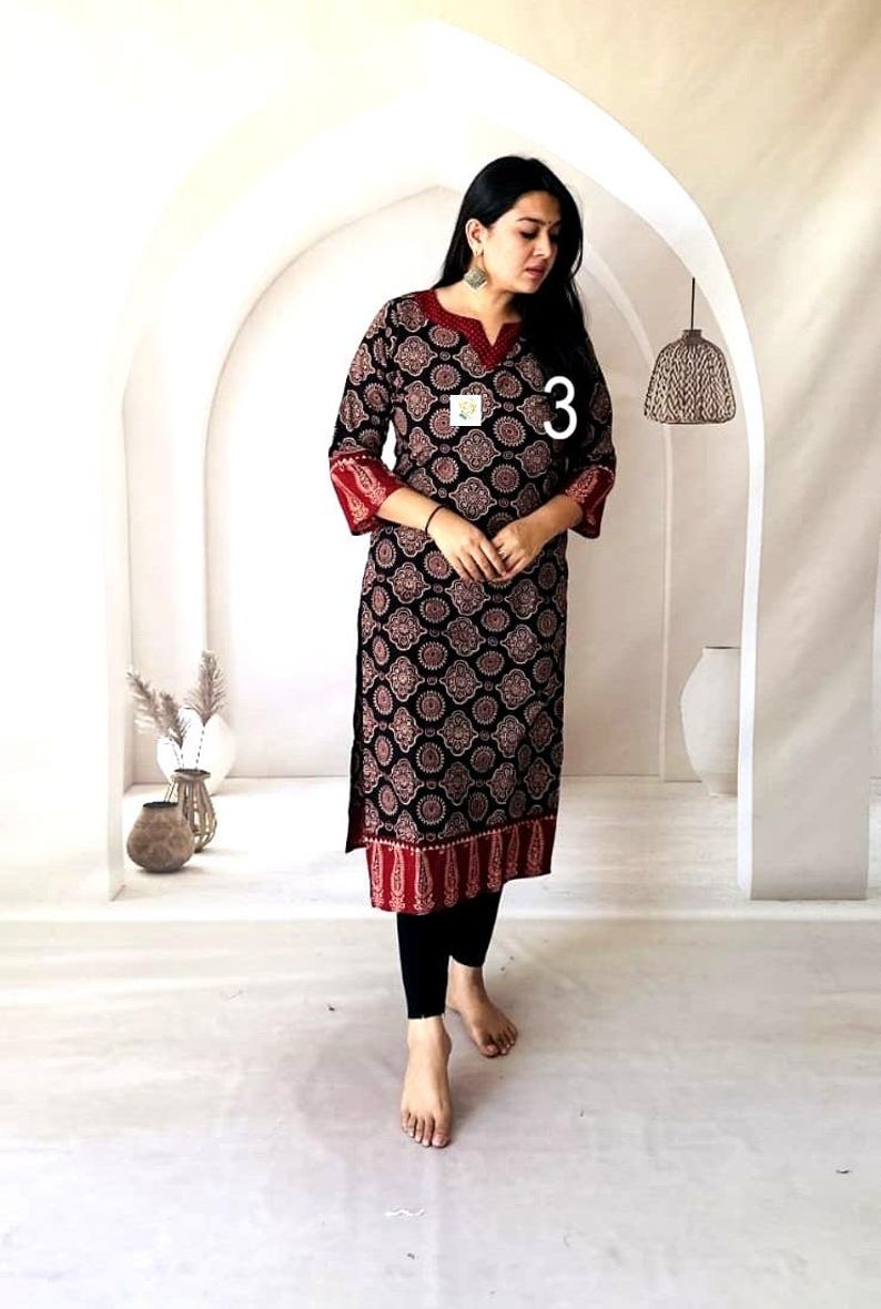 Puede incluir: Una t&uacute;nica negra de manga larga con un estampado circular rojo y blanco. La t&uacute;nica tiene ribetes rojos en las mangas y el dobladillo. El n&uacute;mero "3" es visible en la t&uacute;nica. La persona lleva leggings negros.