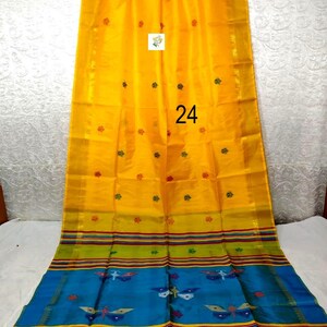 Puede incluir: Un sari de color amarillo brillante con peque&ntilde;os motivos florales rojos y verdes, con un borde ancho que contiene rayas horizontales en verde, rojo y azul. La secci&oacute;n azul muestra patrones de mariposas. El n&uacute;mero 24 est&aacute; impreso en la tela.