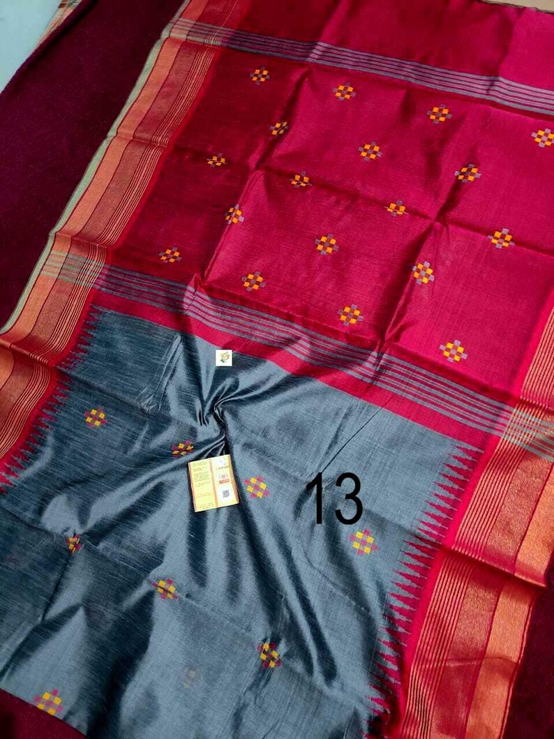 May include: A colourful textile with red and grey sections. The fabric is decorated with small, repeating floral patterns in yellow and orange. The number "13" is visible on the grey section. The edges have striped borders.