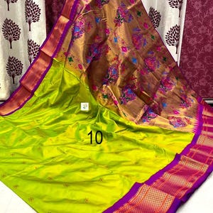 Op de afbeelding: Een limoengroene sari met een grote, metallic gouden pallu met kleurrijke bloemen- en pauwenmotieven. De stof heeft een brede, levendige paarse rand met ingewikkelde gouden geometrische patronen en kleine verspreide bloemaccenten. Het getal 10 is zichtbaar.