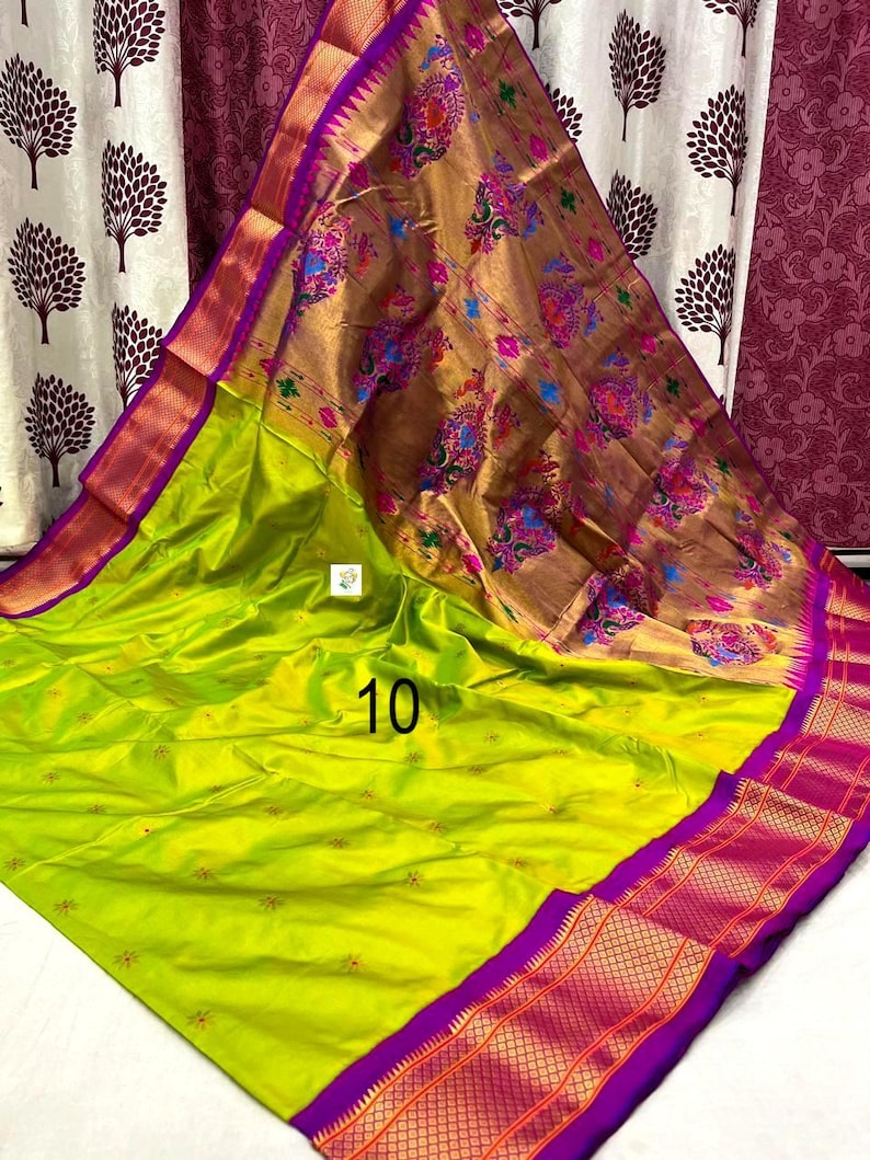 Op de afbeelding: Een limoengroene sari met een grote, metallic gouden pallu met kleurrijke bloemen- en pauwenmotieven. De stof heeft een brede, levendige paarse rand met ingewikkelde gouden geometrische patronen en kleine verspreide bloemaccenten. Het getal 10 is zichtbaar.