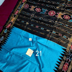 May include: A vibrant textile with a black patterned top and a bright turquoise bottom. The black section features floral and geometric designs in red, yellow, and blue. The number "21" is visible on the turquoise section.