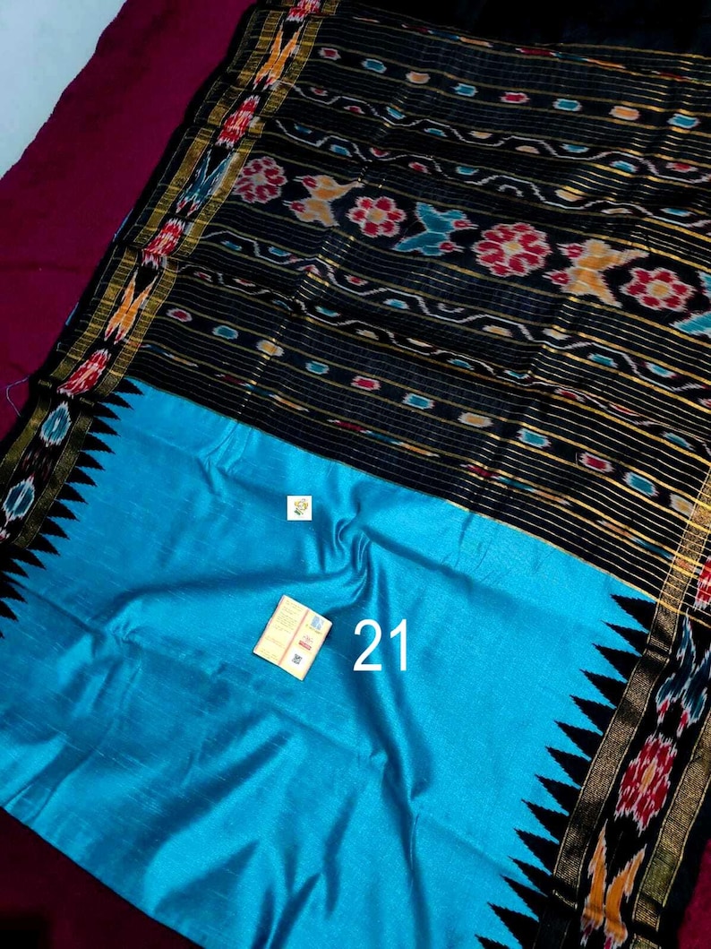 May include: A vibrant textile with a black patterned top and a bright turquoise bottom. The black section features floral and geometric designs in red, yellow, and blue. The number "21" is visible on the turquoise section.