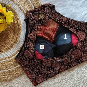 Puede incluir: Una blusa sin mangas de color negro y rojo con un patr&oacute;n y un escote en forma de ojo de cerradura en la espalda. La blusa tiene un cuello alto y una silueta ajustada.