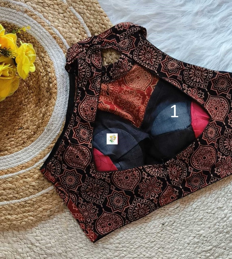 Puede incluir: Una blusa sin mangas de color negro y rojo con un patr&oacute;n y un escote en forma de ojo de cerradura en la espalda. La blusa tiene un cuello alto y una silueta ajustada.